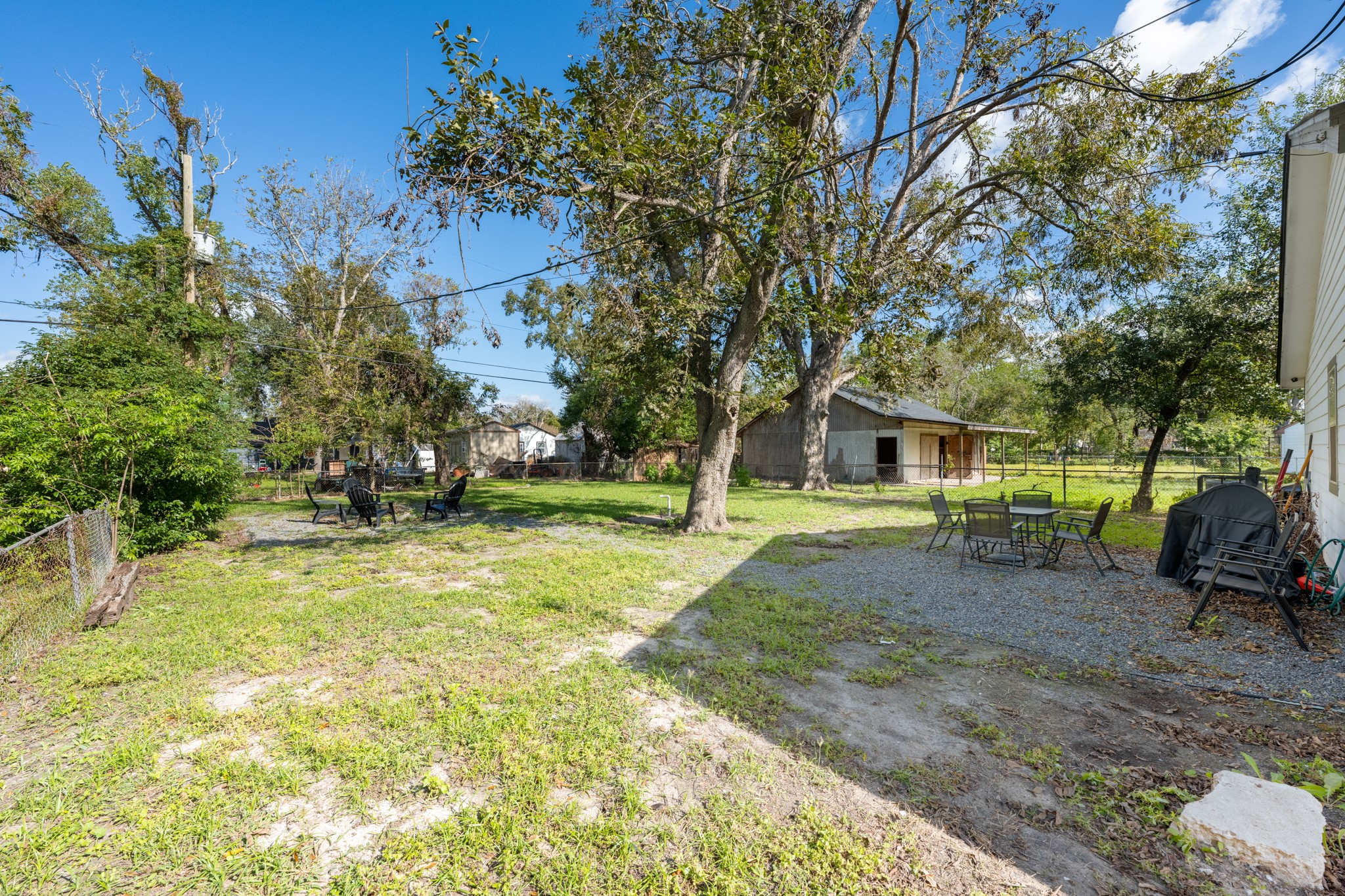 729 Kyle Angleton, TX 77515 - Photo 33 of 36 Spacious backyard with mature trees, a gravel patio area featuring outdoor seating, offering a mix of greenery and functional outdoor space.