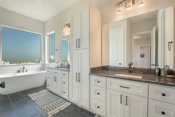 a bathroom with a granite countertop double vanity sink large mirror and bathtub