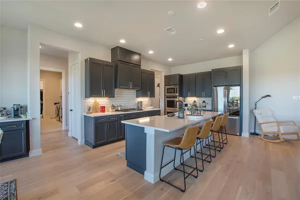 a room with stainless steel appliances kitchen island granite countertop a table chairs and a refrigerator