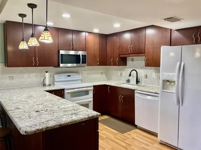 a kitchen with stainless steel appliances granite countertop wooden cabinets a refrigerator a stove a sink and a oven