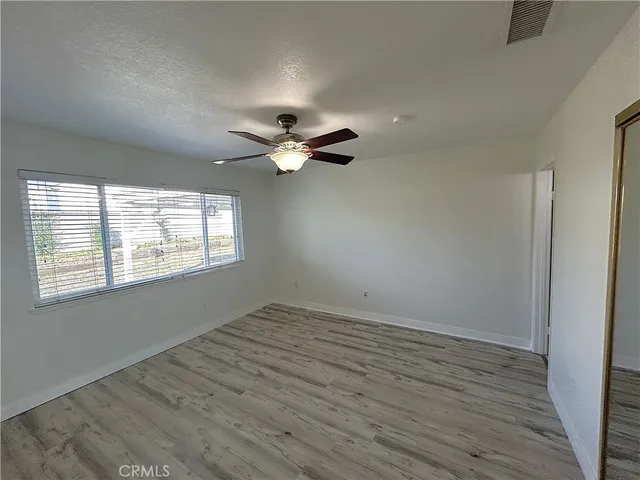 an empty room with wooden floor fan and windows