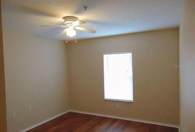 an empty room with wooden floor fan and windows