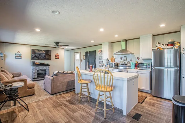 a kitchen with stainless steel appliances kitchen island granite countertop a refrigerator a stove a sink a dining table and chairs with wooden floor