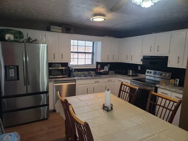 a kitchen with granite countertop a refrigerator a stove a sink dishwasher and white cabinets with wooden floor