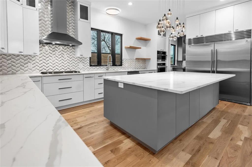 309 Kaye Street Coppell, TX 75019 - Photo 35 of 36 Contemporary kitchen featuring a spacious center island with a white countertop, stainless steel appliances, herringbone pattern backsplash, light wood-finish flooring, and minimalist cabinetry