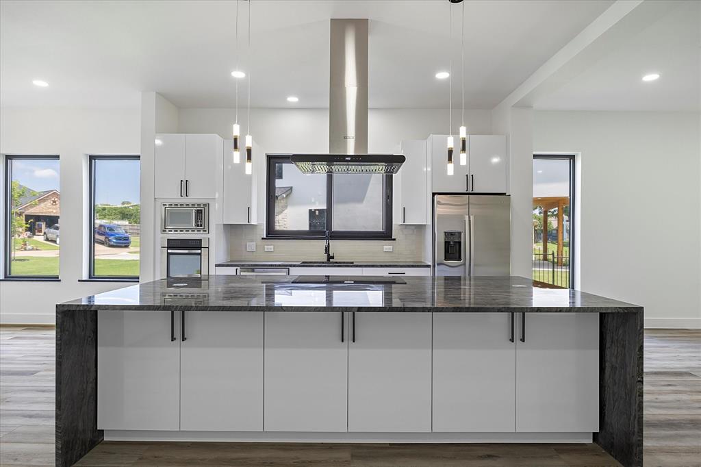 2811 Rodeo Drive Quinlan, TX 75474 - Photo 4 of 35 Kitchen with stainless steel appliances, range hood, white cabinets, a large island, and tasteful backsplash