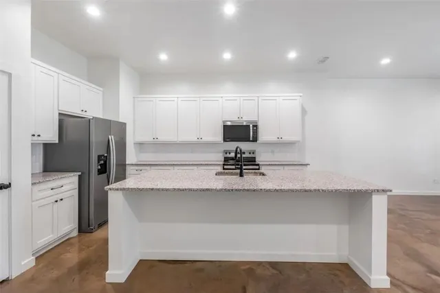 a large kitchen with kitchen island a sink dishwasher a refrigerator and white cabinets with wooden floor
