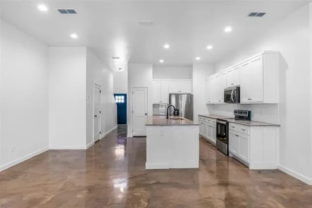 a large white kitchen with stainless steel appliances granite countertop a stove a sink a refrigerator and white cabinets with wooden floor