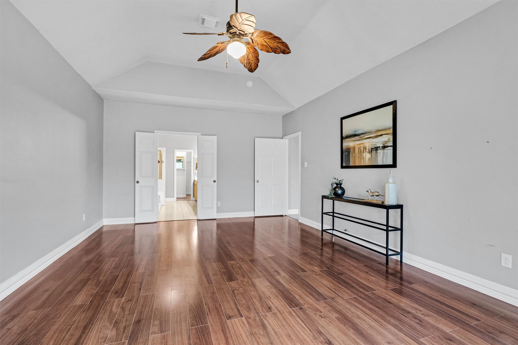 23 Alba Road Montgomery, TX 77356 - Photo 18 of 37 Spacious room with high vaulted ceiling, featuring wood flooring and neutral gray walls. A ceiling fan adds charm, and double doors open to an adjacent area. A sleek console table and artwork enhance the modern aesthetic.