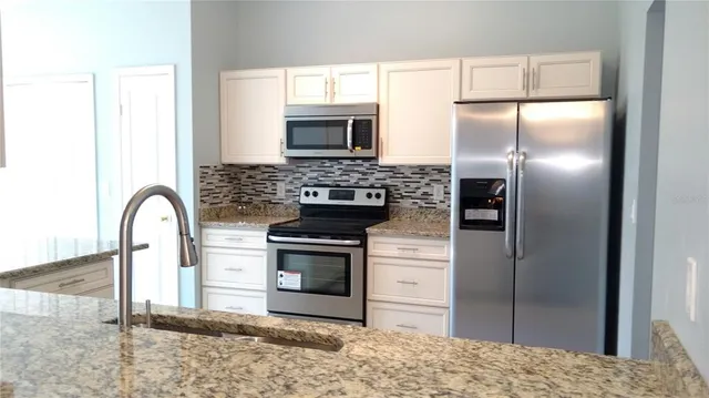 a kitchen with stainless steel appliances granite countertop a refrigerator a stove and a sink