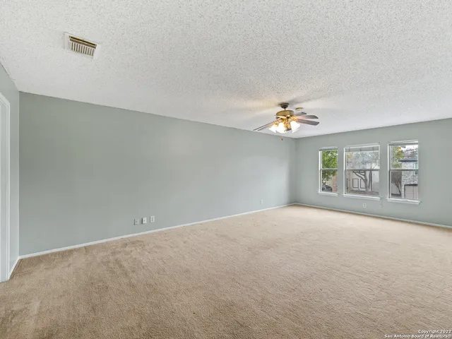 an empty room with a chandelier fan and windows
