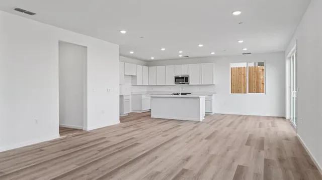 a view of an empty room with wooden floor and kitchen