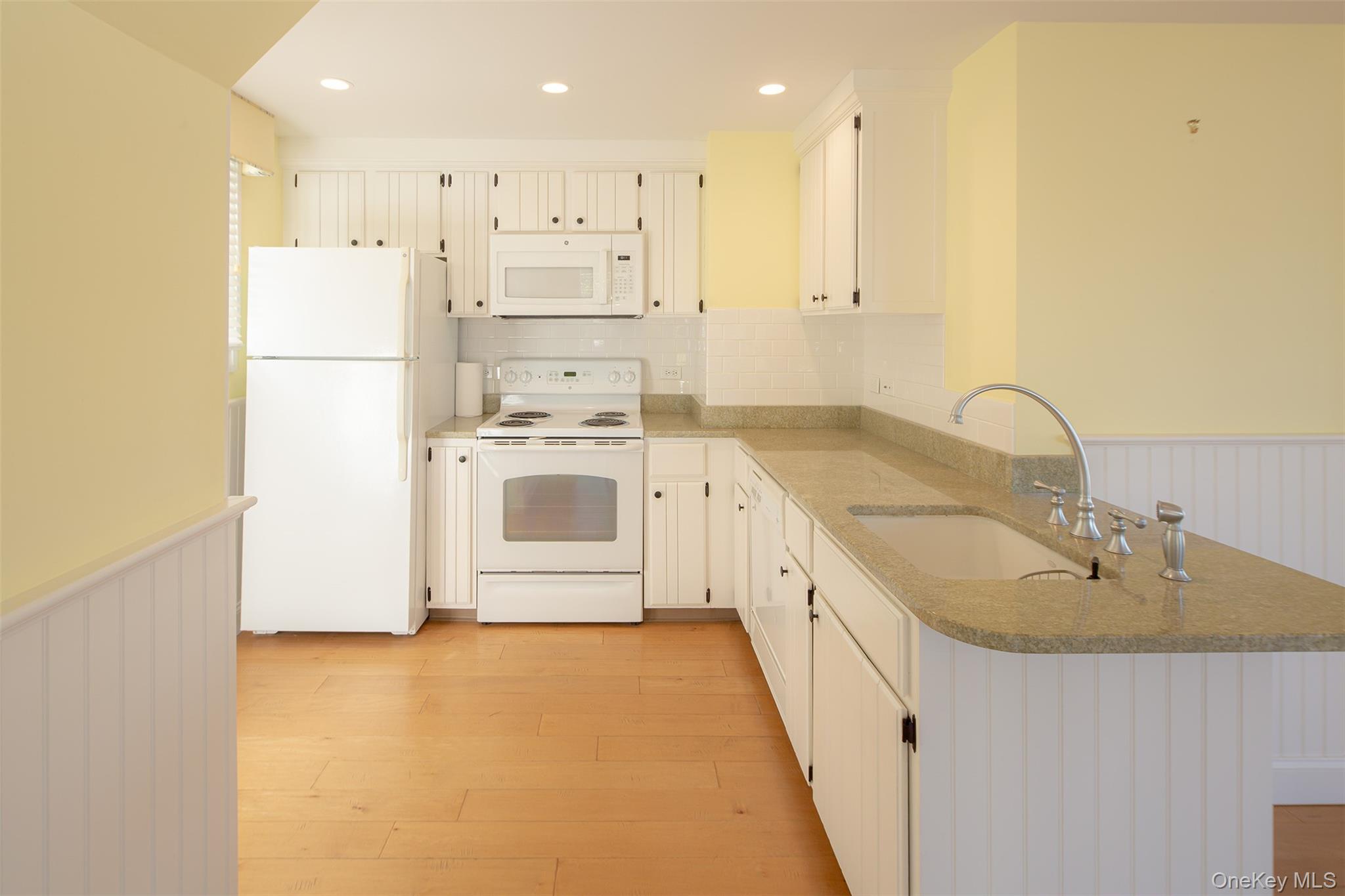 1 Canal Road Hampton Bays, NY 11946 - Photo 11 of 50 Kitchen with a wainscoted wall, white appliances, light stone countertops, decorative backsplash, and light wood-style floors