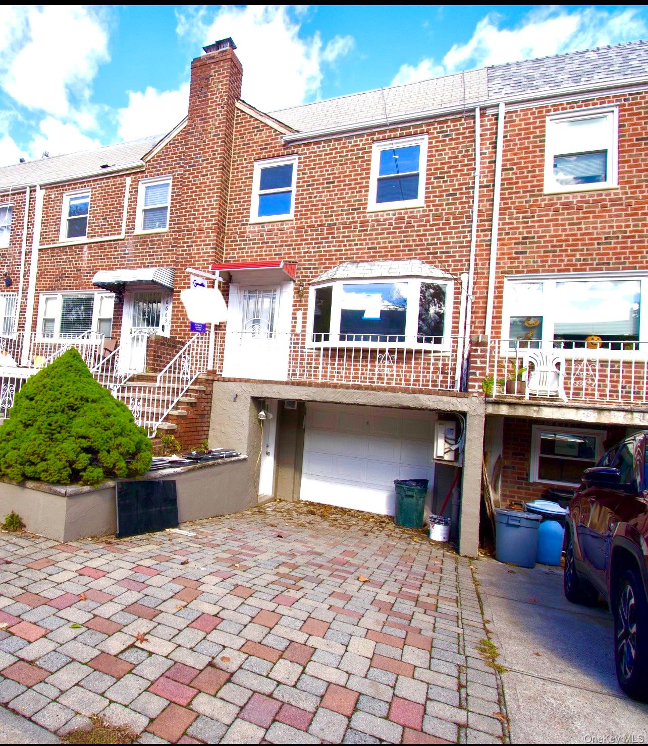 View of front facade featuring brick siding, decorative driveway, a residential view, a chimney, and a garage