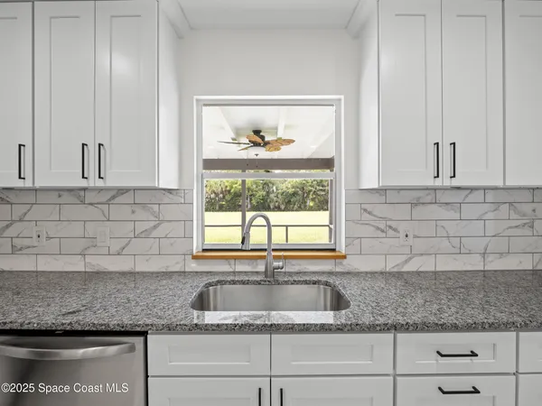 a large white kitchen with a stove a sink dishwasher and a refrigerator with white cabinets