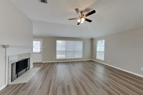 an empty room with wooden floor fireplace and windows