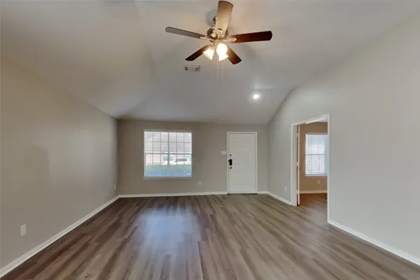an empty room with wooden floor ceiling fan and windows