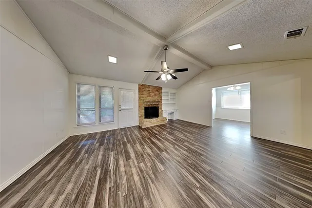 an empty room with wooden floor fireplace and windows