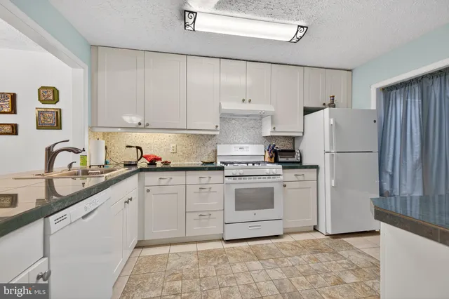 a kitchen with granite countertop a refrigerator sink stove and white cabinets