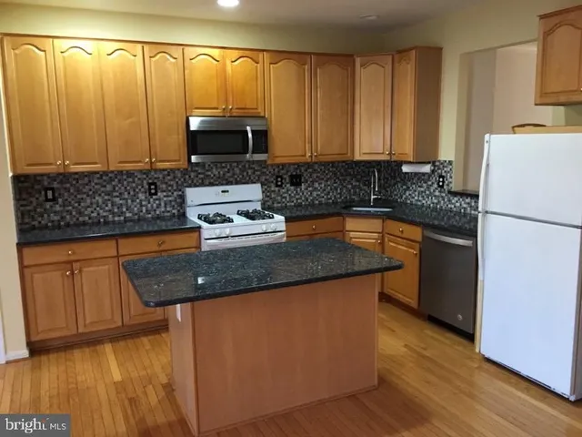 a kitchen with granite countertop wood cabinets stainless steel appliances and a wooden floor