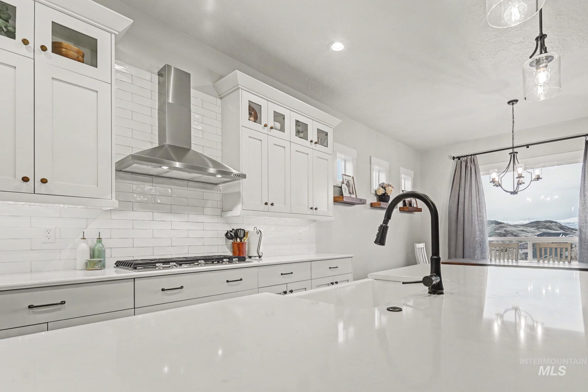 18357 North Burnt Car Way Boise, ID 83714 - Photo 14 of 48 Kitchen featuring glass fronted cabinets, white cabinetry, light stone countertops, decorative backsplash, and suspended lighting