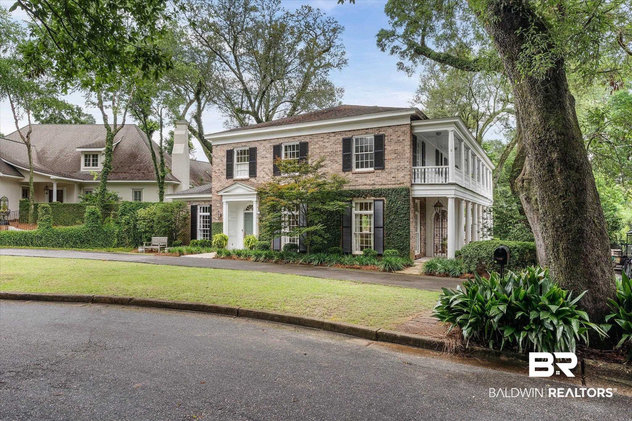 3908 Yester Place Mobile, AL 36608 - Photo 42 of 45 Two-story brick residence featuring white columns, a second-story balcony with railing, black louvered shutters, and a front entry with a portico