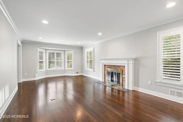 an empty room with wooden floor fireplace and windows