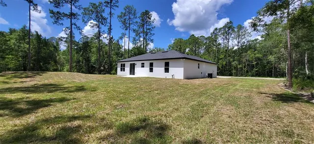 a white house with a big yard plants and large trees