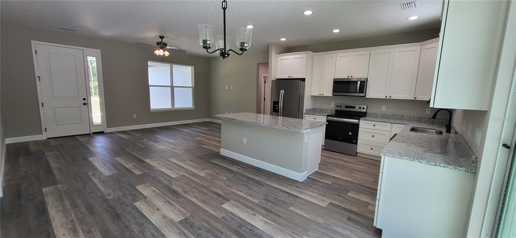1666 Berrybush Street Bunnell, FL 32110 - Photo 5 of 26 a large kitchen with stainless steel appliances granite countertop a stove a sink dishwasher and a refrigerator with wooden floor
