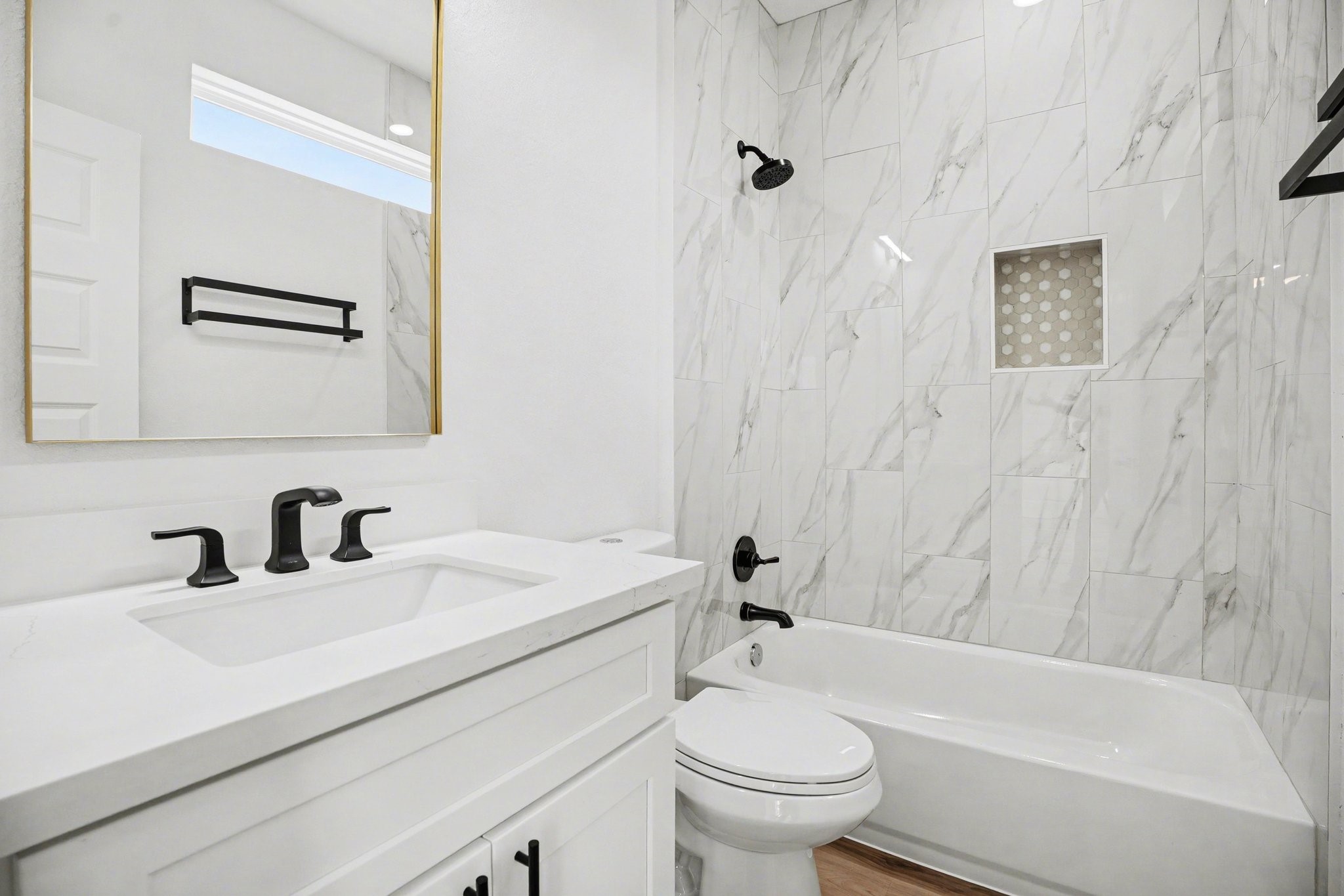 115 Milby Street Houston, TX 77003 - Photo 24 of 28 This modern bathroom features sleek white marble tile, a bathtub with a shower, and contemporary black fixtures. The vanity includes a large mirror and ample storage, creating a clean and elegant space.