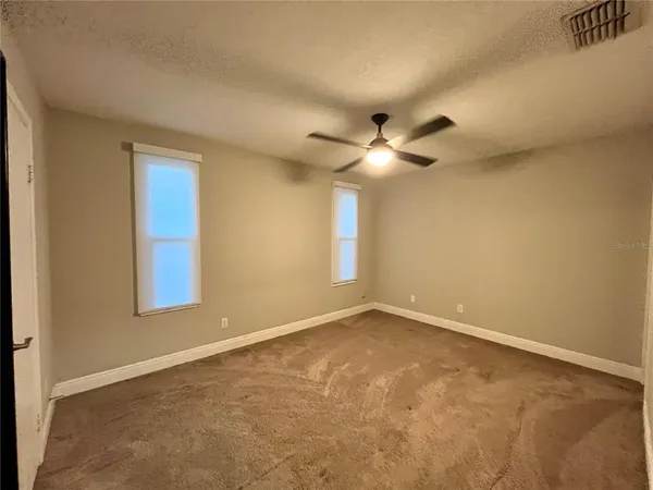 an empty room with a chandelier fan and windows