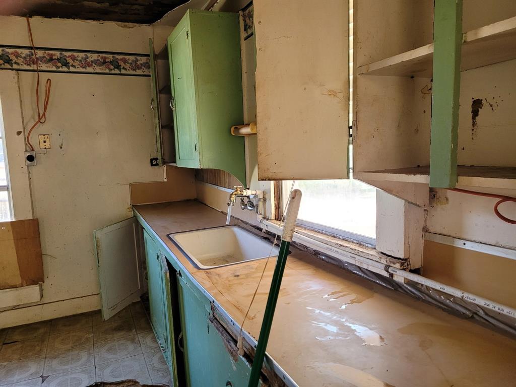 909 Ivan Road Waco, TX 76706 - Photo 8 of 10 Kitchen space featuring a window, overhead cabinetry, base cabinetry, an integrated sink, and an exposed pipe