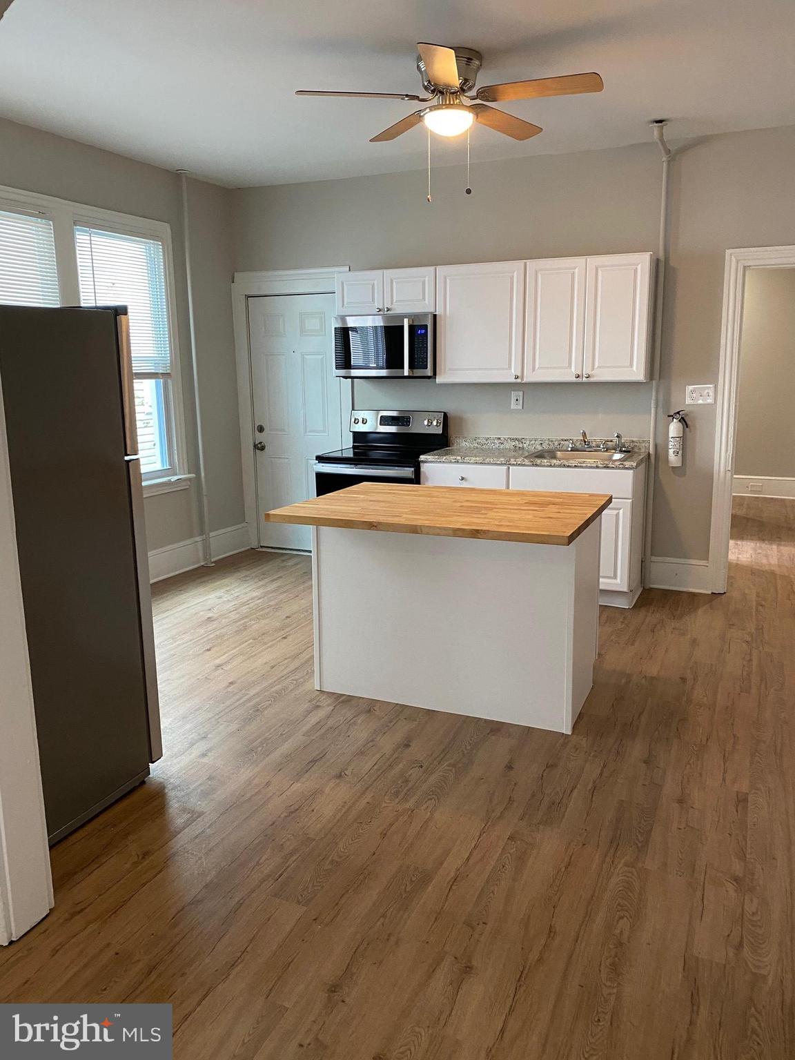 a large kitchen with stainless steel appliances granite countertop a refrigerator a sink a stove a microwave and island with wooden floor