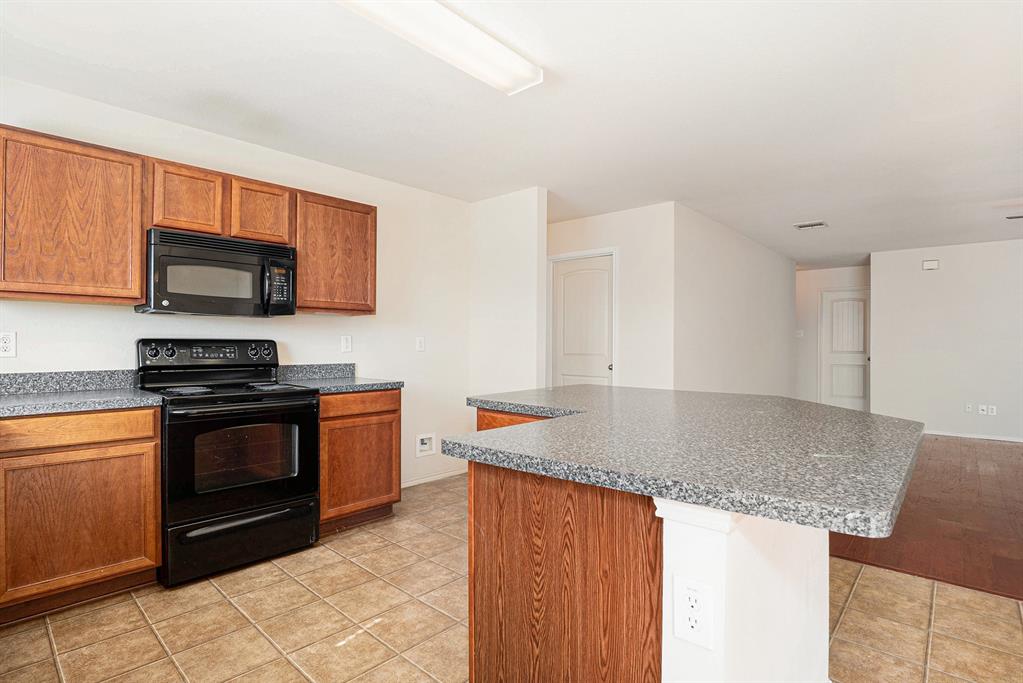 2120 Bliss Road Fort Worth, TX 76177 - Photo 13 of 25 Kitchen with black appliances, light tile patterned floors, wood finish cabinetry, a kitchen island, and dark countertops