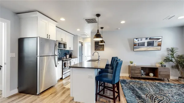 a kitchen with stainless steel appliances granite countertop a refrigerator a stove a sink a dining table and chairs with wooden floor