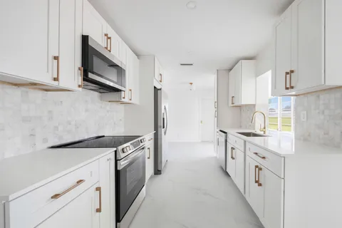 a kitchen with stainless steel appliances granite countertop white cabinets a sink a stove a microwave and a refrigerator