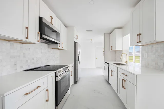 a kitchen with stainless steel appliances granite countertop white cabinets a sink a stove a microwave and a refrigerator