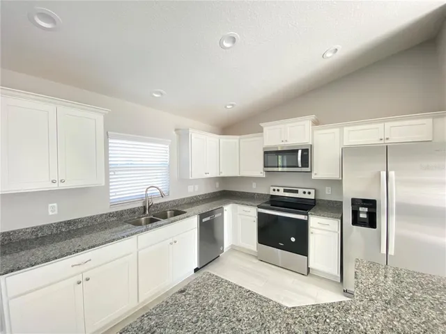 a kitchen with stainless steel appliances granite countertop a sink a stove a refrigerator and white cabinets