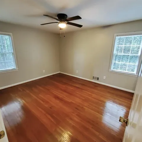 an empty room with wooden floor fan and windows