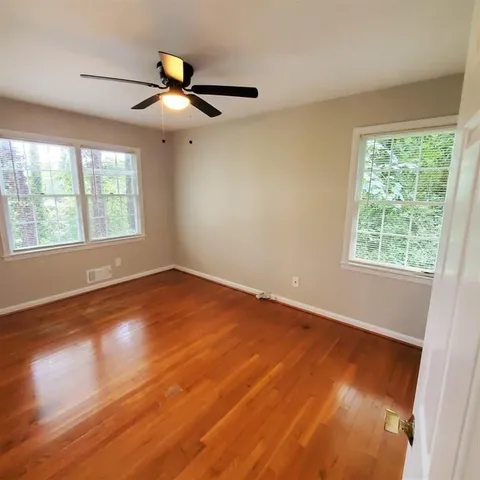 an empty room with wooden floor fan and windows