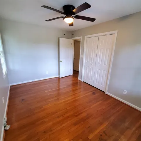 an empty room with wooden floor ceiling fan and windows
