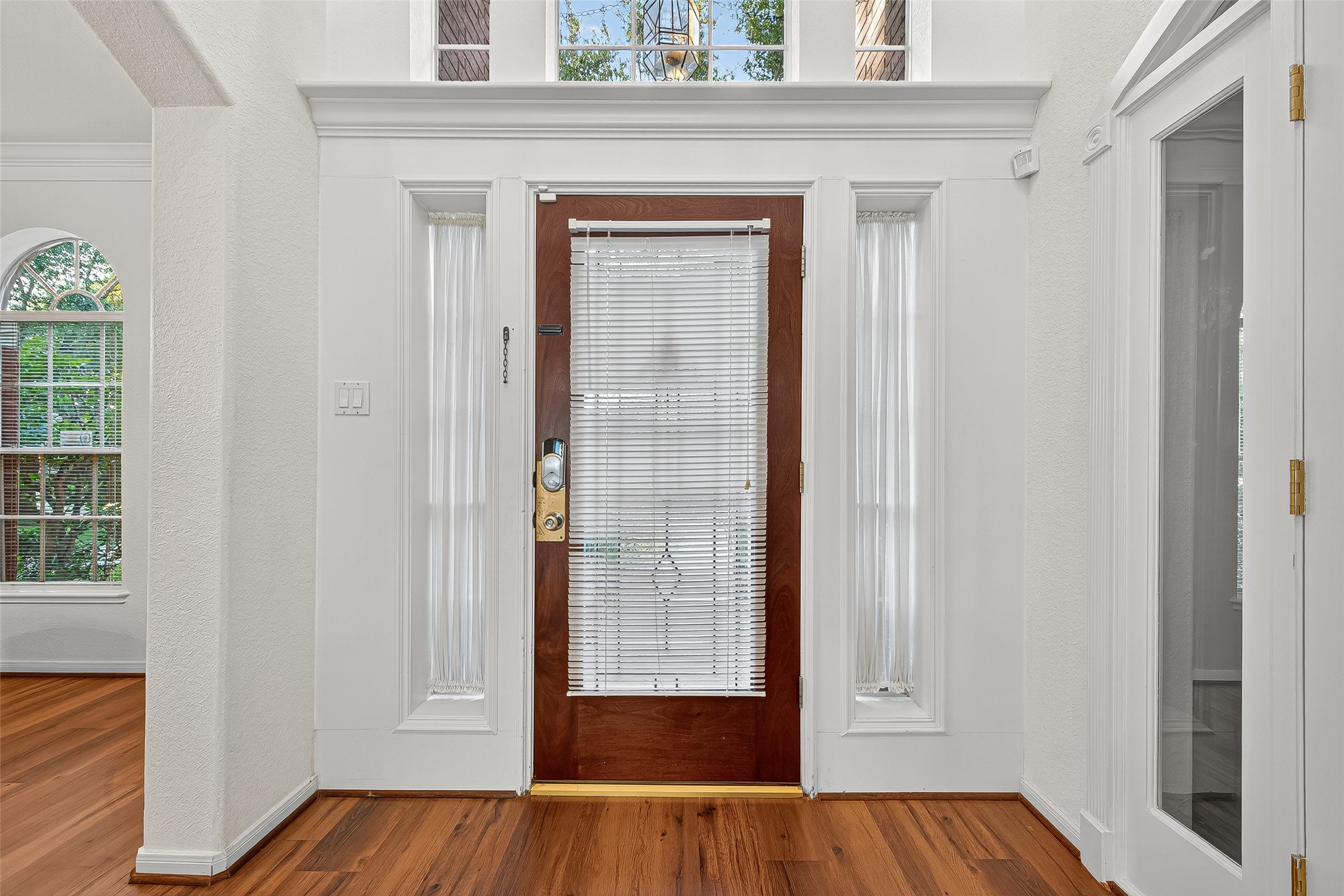13011 Mossy Ridge Cove Houston, TX 77041 - Photo 7 of 50 This photo showcases a bright entryway with a wooden door featuring glass panels and blinds. Flanked by tall windows, it allows natural light to fill the space.