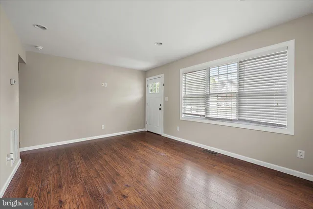 a view of an empty room with wooden floor and a window