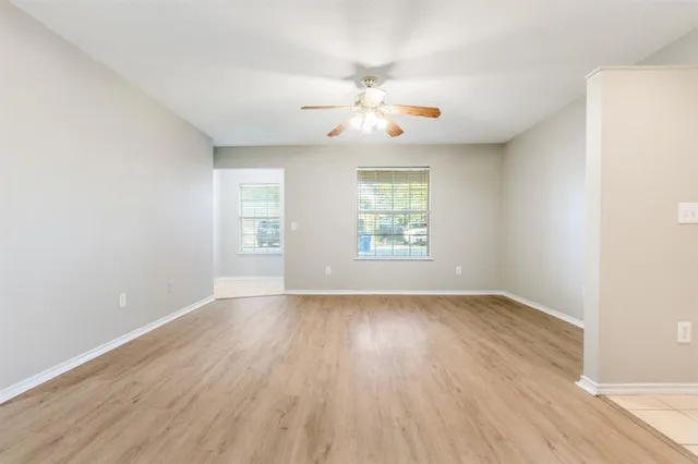 an empty room with wooden floor chandelier fan and windows