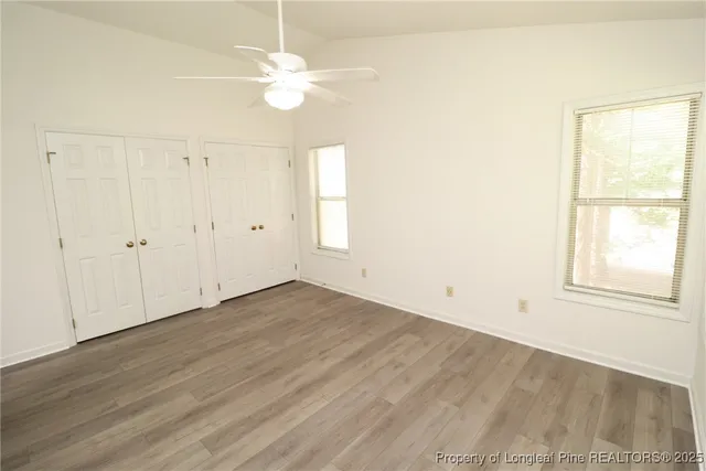 an empty room with wooden floor fan and windows