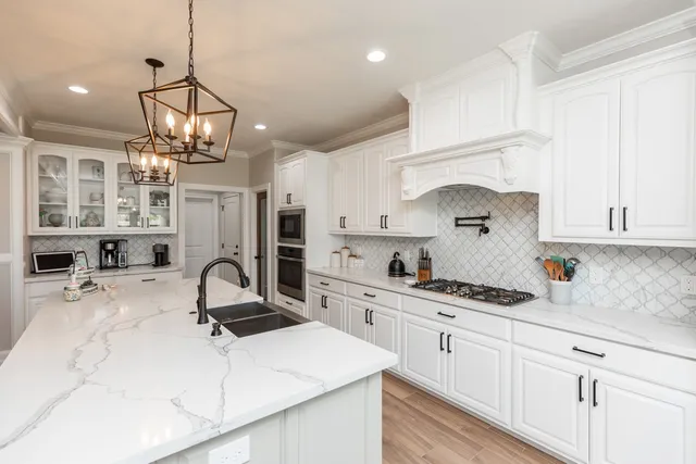 a kitchen with kitchen island stainless steel appliances a sink stove and white cabinets with wooden floor