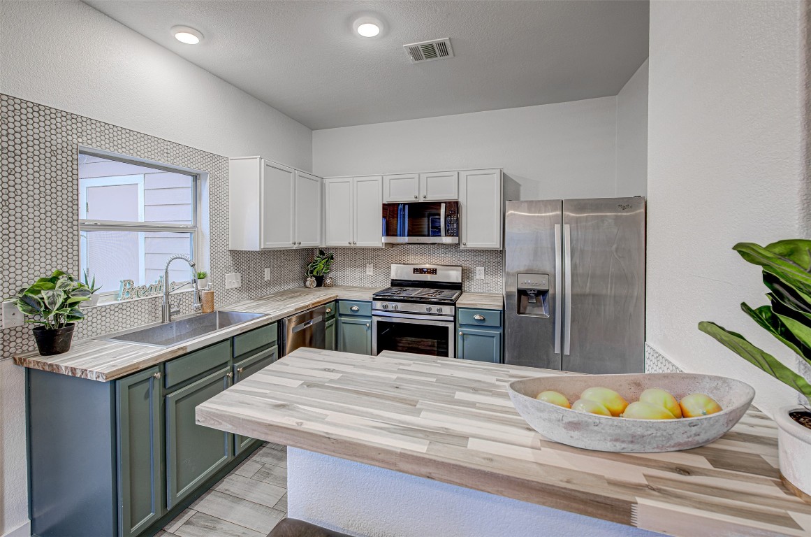 6249 Negley, Unit B Kyle, TX 78640 - Photo 1 of 26 Kitchen with appliances with stainless steel finishes, white cabinetry, wood counters, blue cabinetry, and backsplash