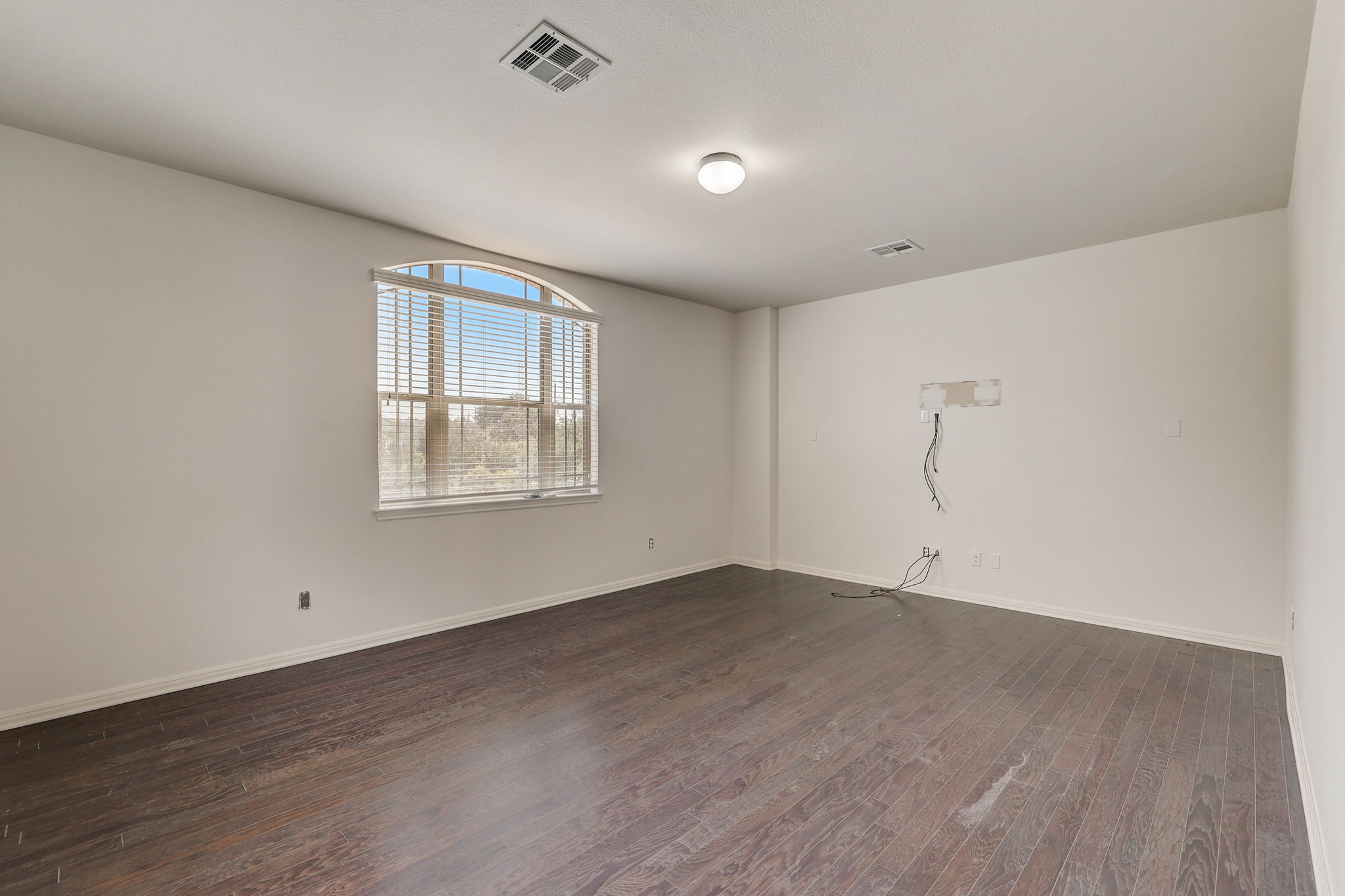 16012 Spillman Ranch Loop Austin, TX 78738 - Photo 27 of 38 Rich hardwood flooring creates a refined backdrop for a spacious room featuring a graceful arched window.