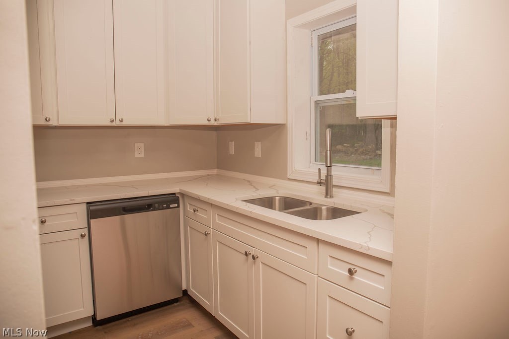 3644 Padanarum Road Geneva, OH 44041 - Photo 6 of 19 Kitchen featuring white shaker-style cabinetry, light-toned countertops, a stainless steel dishwasher, a double basin sink with a gooseneck faucet, and wood-finish flooring