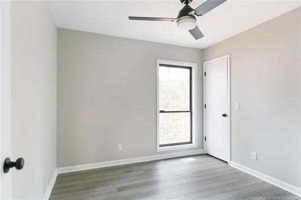 an empty room with wooden floor ceiling fan and windows